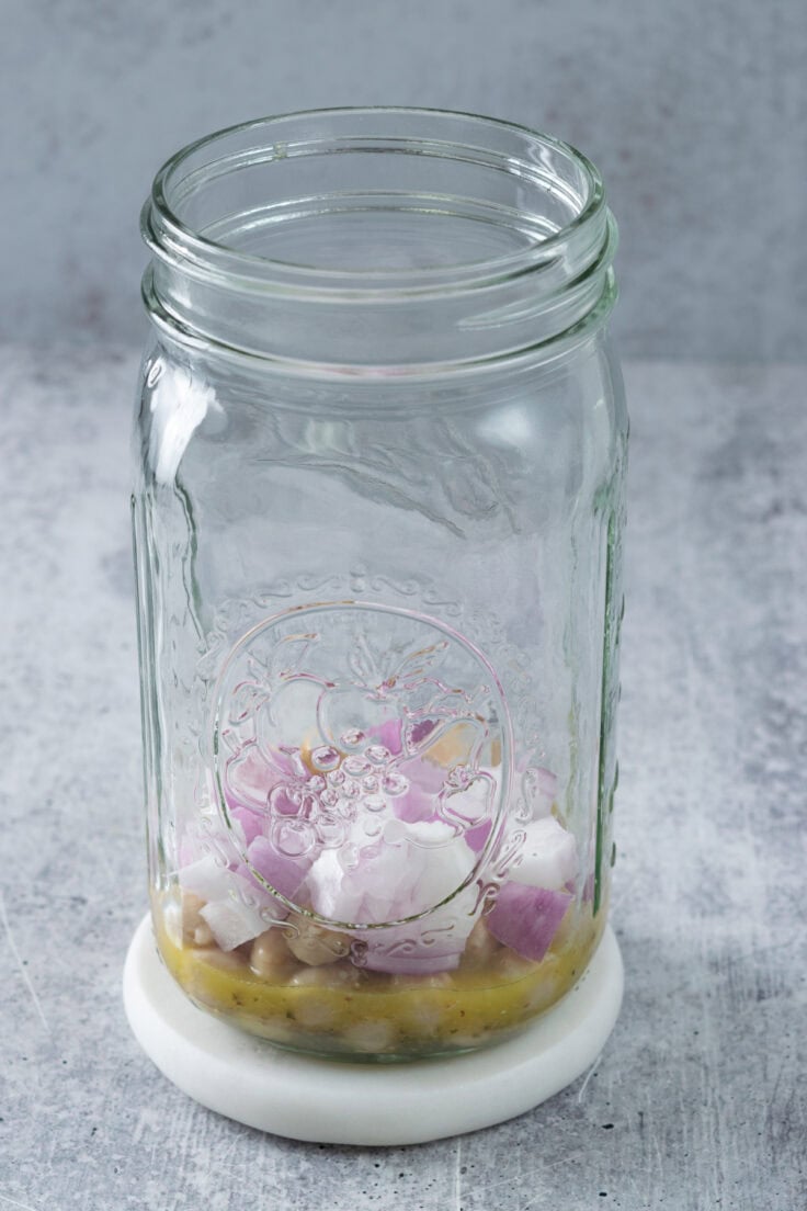 Lemon dressing, chickpeas and chopped red onion in a mason jar to make Mediterranean salad.