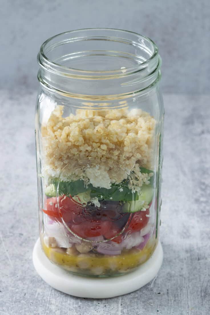 Cooked quinoa layered on top of other Mediterranean salad in a jar ingredients.