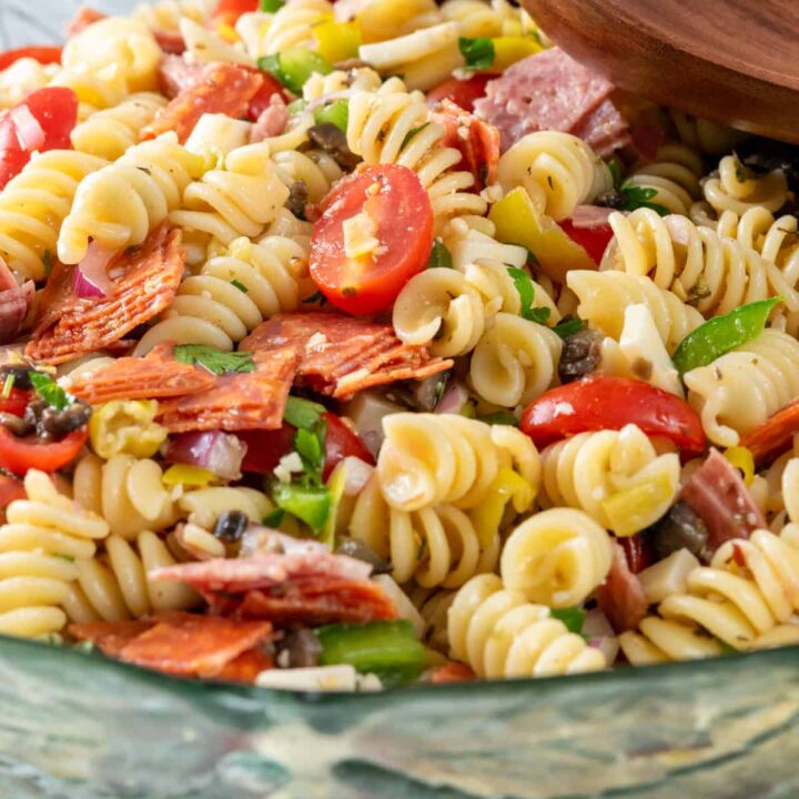 A big bowl of Italian pasta salad with rotini noodles, salami, pepperoni, tomatoes, olive, provolone cheese and more.