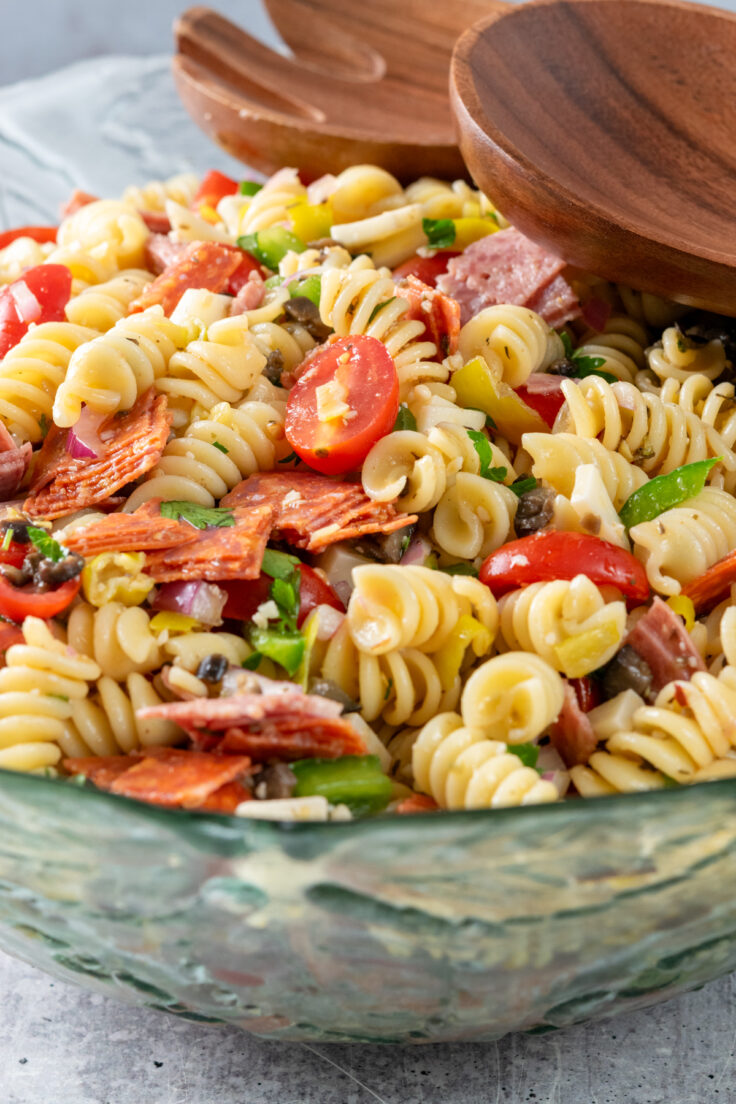 A big bowl of Italian pasta salad with rotini noodles, salami, pepperoni, tomatoes, olive, provolone cheese and more.