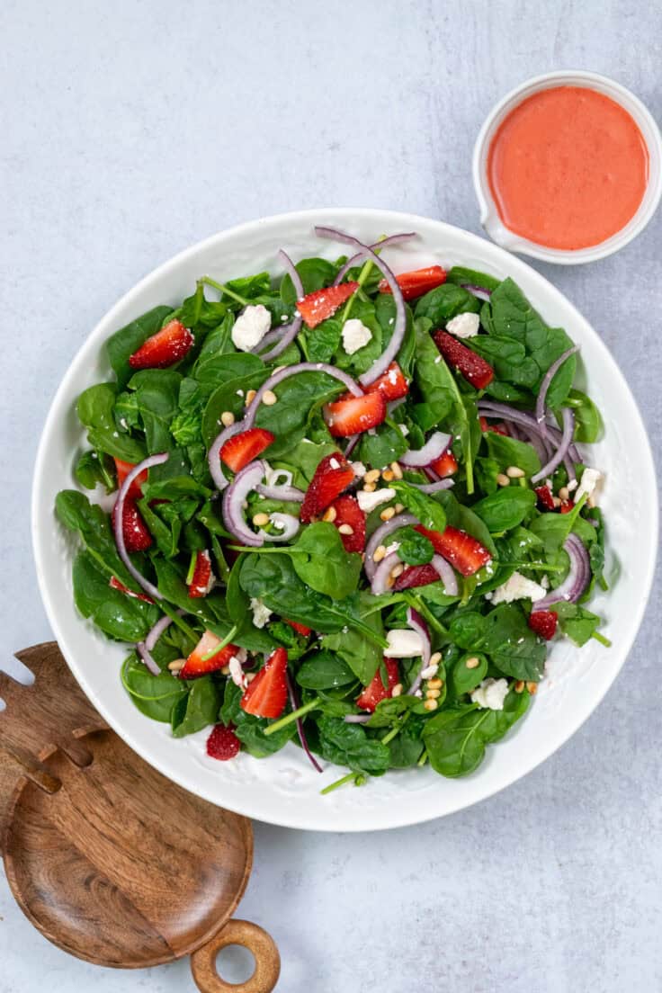 Spinach salad with strawberries all tossed together in a large salad serving bowl.