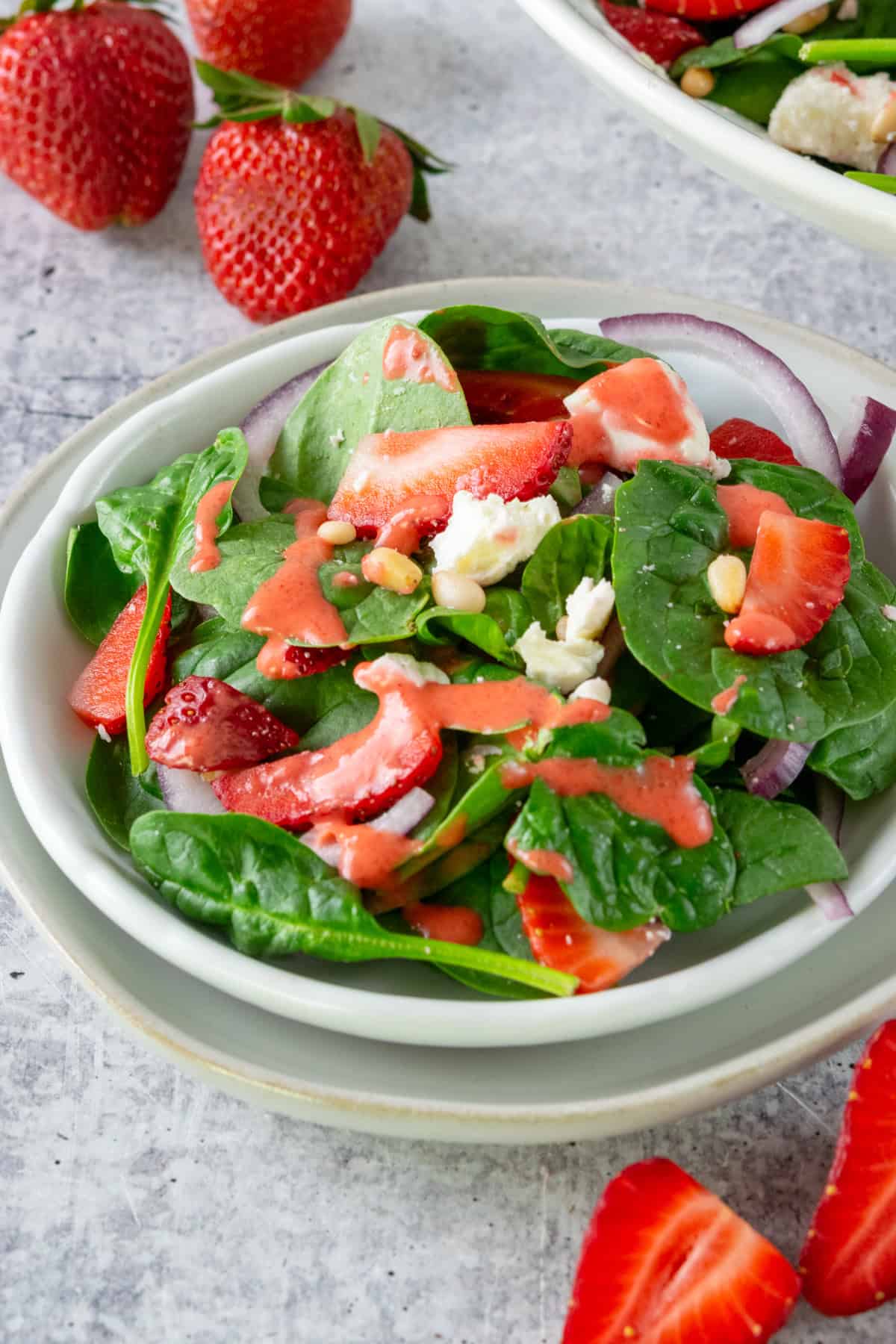 A spinach salad with strawberries and strawberry vinaigrette on a salad plate, which is next to a large bowl full of the strawberry spinach salad.