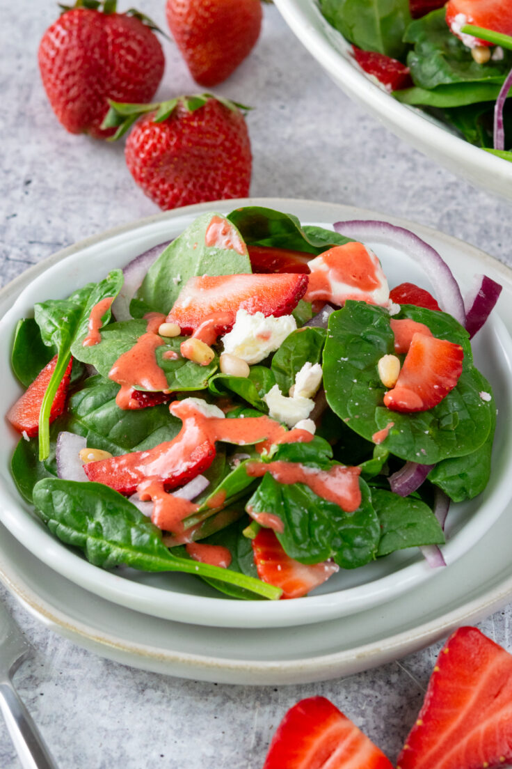 Strawberry vinaigrette dressing drizzled on a on spinach salad side salad.