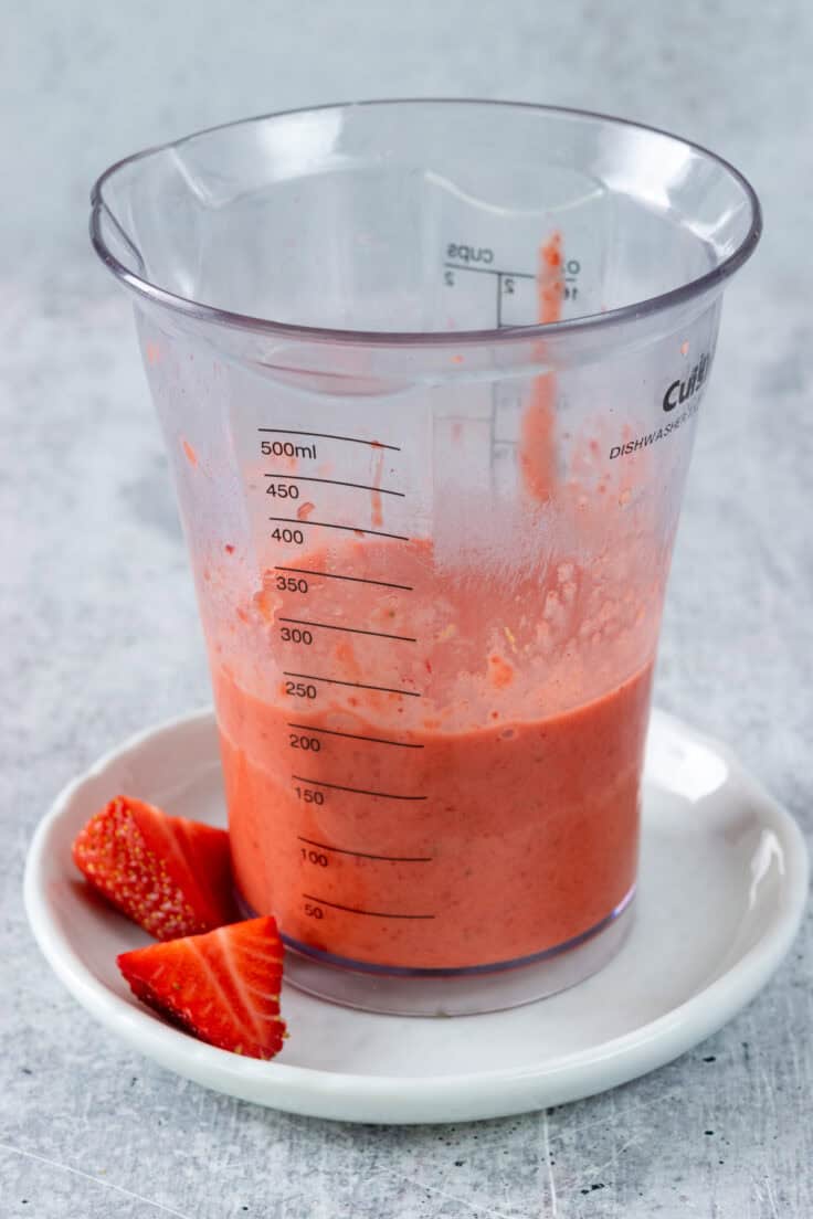 The strawberry vinaigrette has been blended with an immersion blender and is in a tall measuring cup.