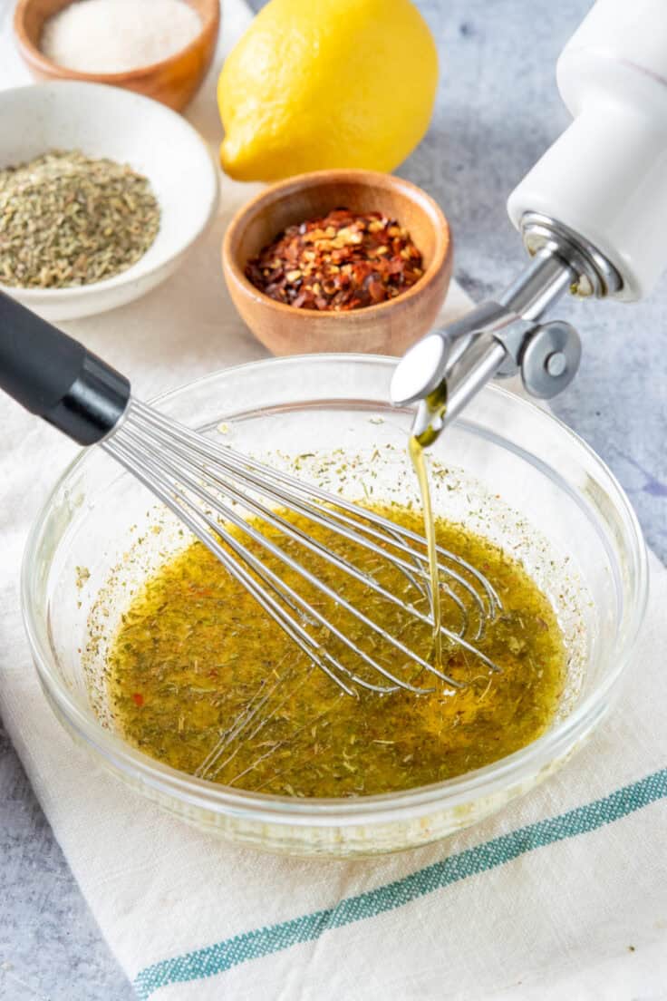 Making homemade Italian vinaigrette by drizzling olive oil into vinegar and seasonings while whisking at the same time.