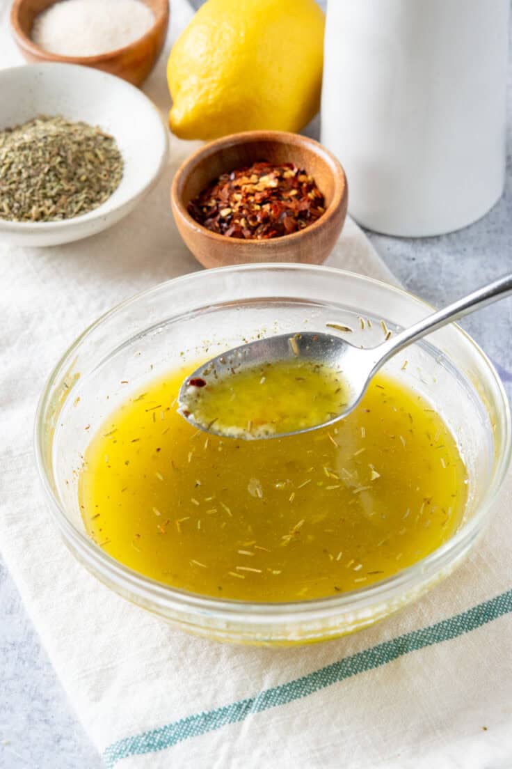 A spoonful of the dressing being held over the bowl it was whisked together in, showing how it is emulsified.