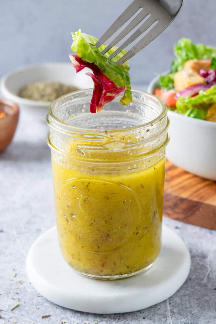 A fork with salad on it being dipped into a jar of homemade Italian dressing.