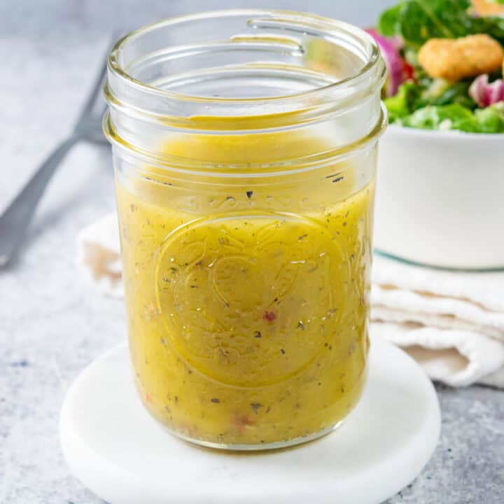 A har of homemade italian vinaigrette dressing next to a salad and fork.