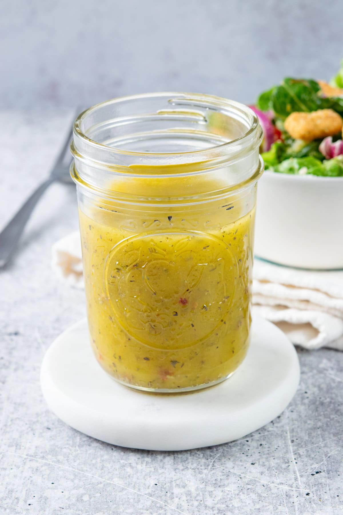 A har of homemade italian vinaigrette dressing next to a salad and fork.