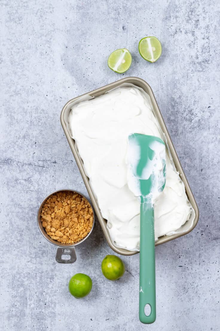 The remaining key lime pie ice cream base is spread into the loaf pan with a green rubber spatula.