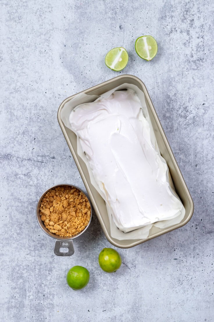 A metal loaf pan that's lined with wax paper and filled with half of the key lime pie ice cream base.