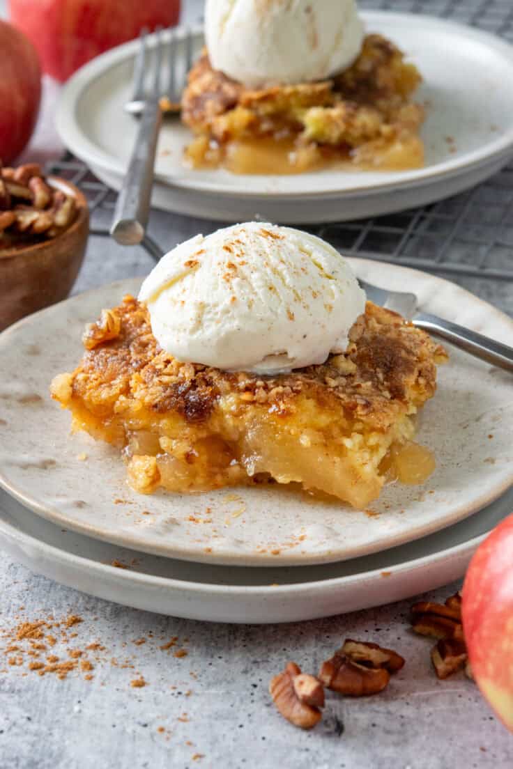Two plates and forks, each with a slice of apple dump cake and scoop of vanilla ice cream dusted with cinnamon on top.