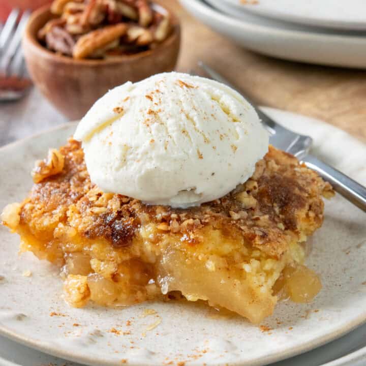 Apple dump cake on a plate topped with vanilla ice cream and cinnamon. Warm apple filling is topped with a buttery cake mix and crunchy pecan and brown sugar topping.