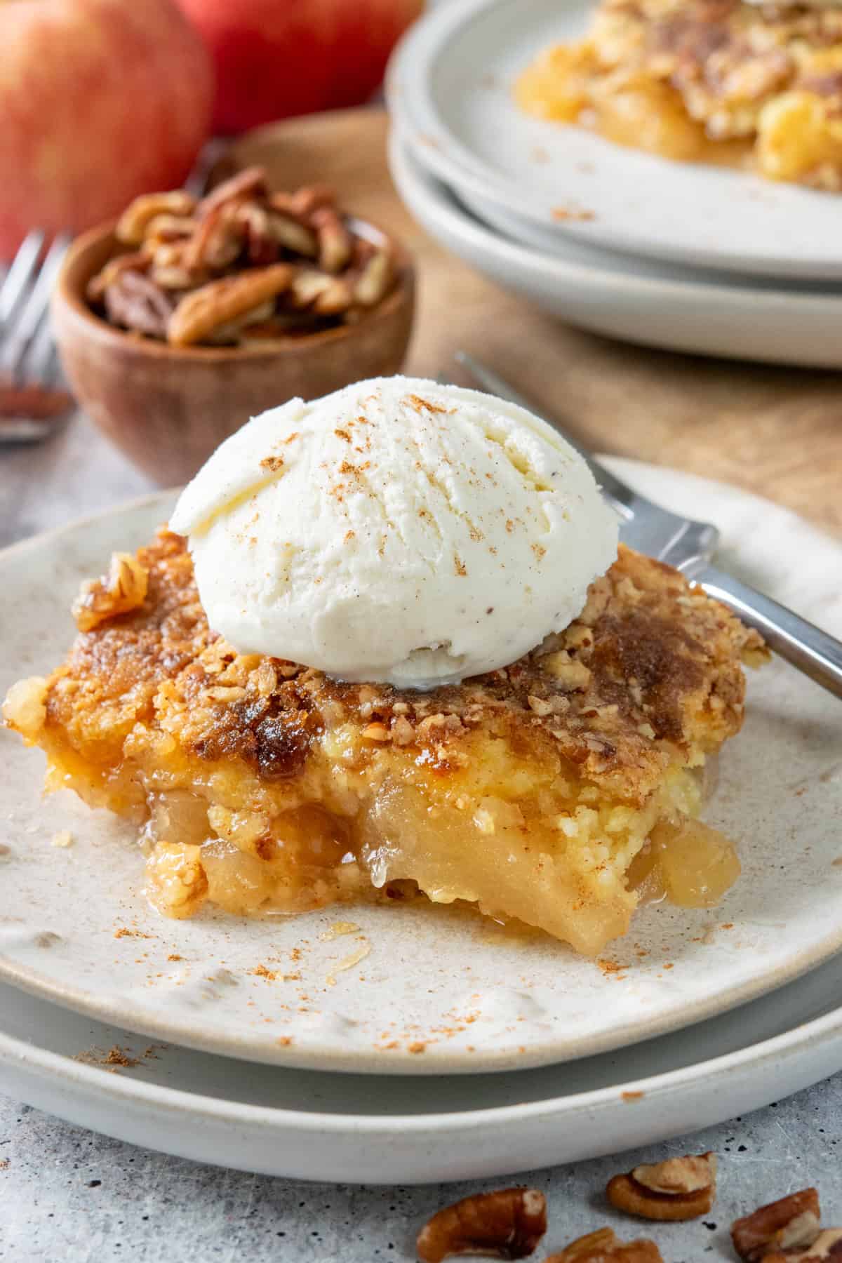 Apple dump cake on a plate topped with vanilla ice cream and cinnamon. Warm apple filling is topped with a buttery cake mix and crunchy pecan and brown sugar topping.