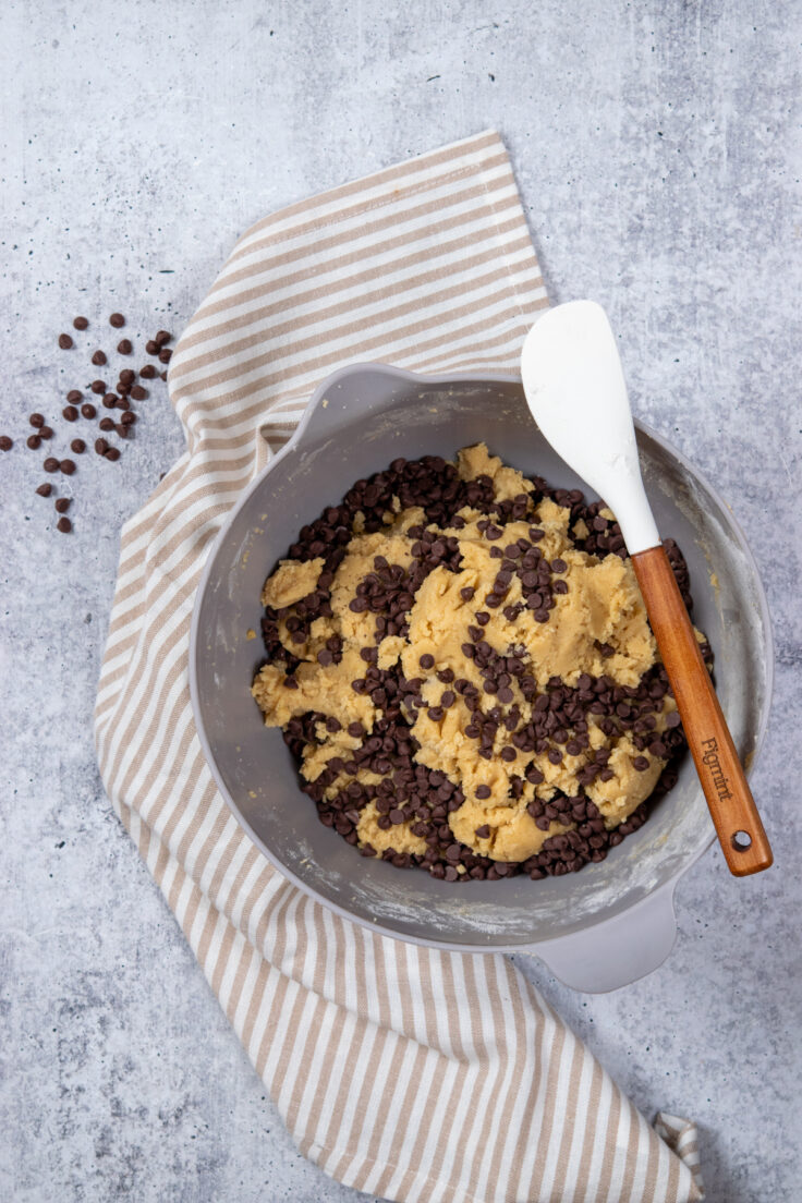 Mixing bowl filled with chocolate chip cookie batter with mini chocolate chips stirred into it.