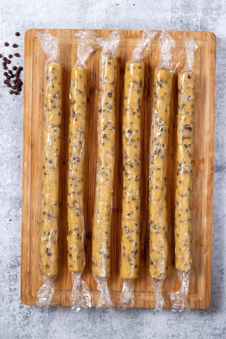 Six long, skinny cough dough logs wrapped in plastic, ready to chill before slicing and baking.
