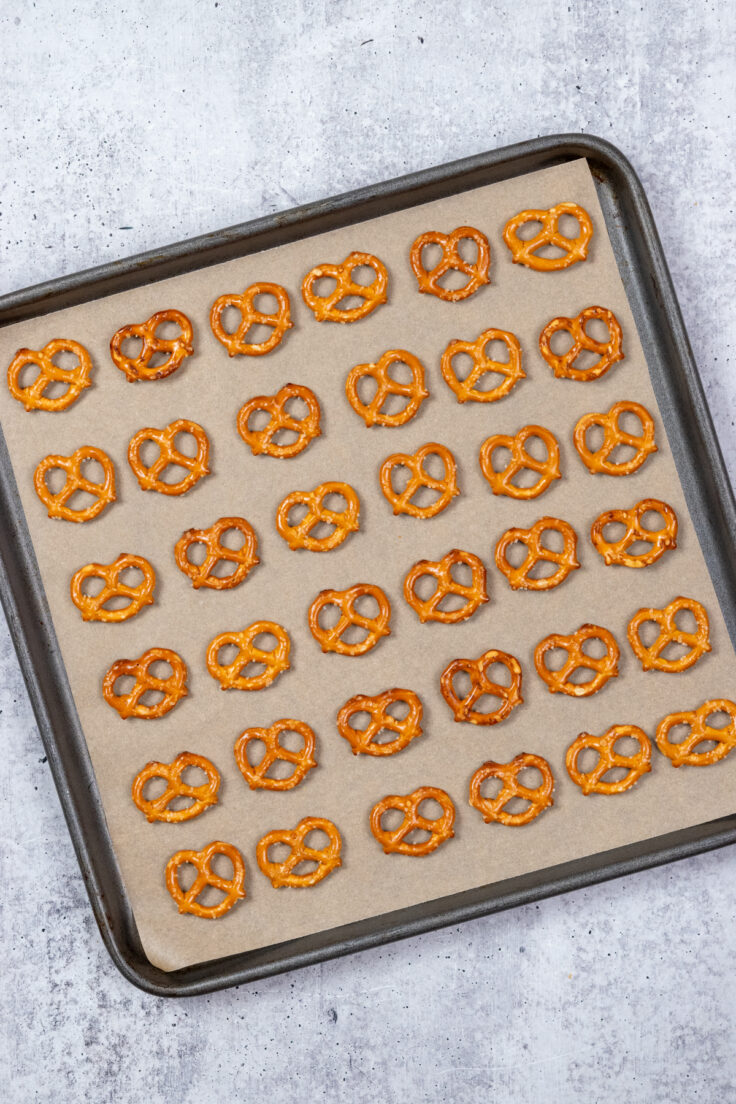 A baking tray lined with parchment paper that has 36 mini pretzels evenly spread out on it.