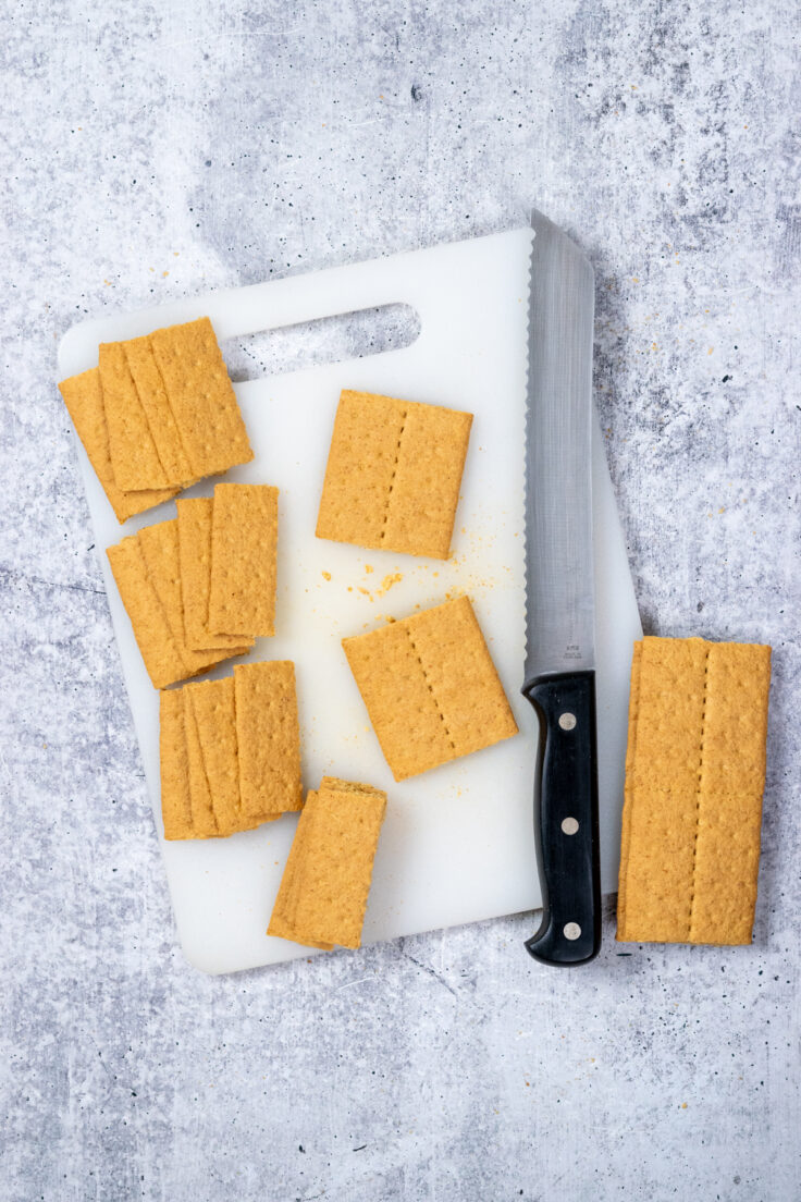 A serrated knife on a cutting board next to sheets of graham crackers that have been cut into four pieces each.