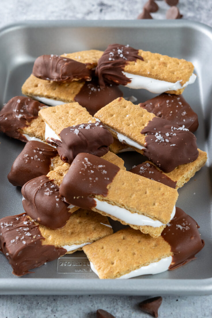 A tray stacked high with smores bites filled with marshmallow fluff, dipped in chocolate, and topped with flaky sea salt.