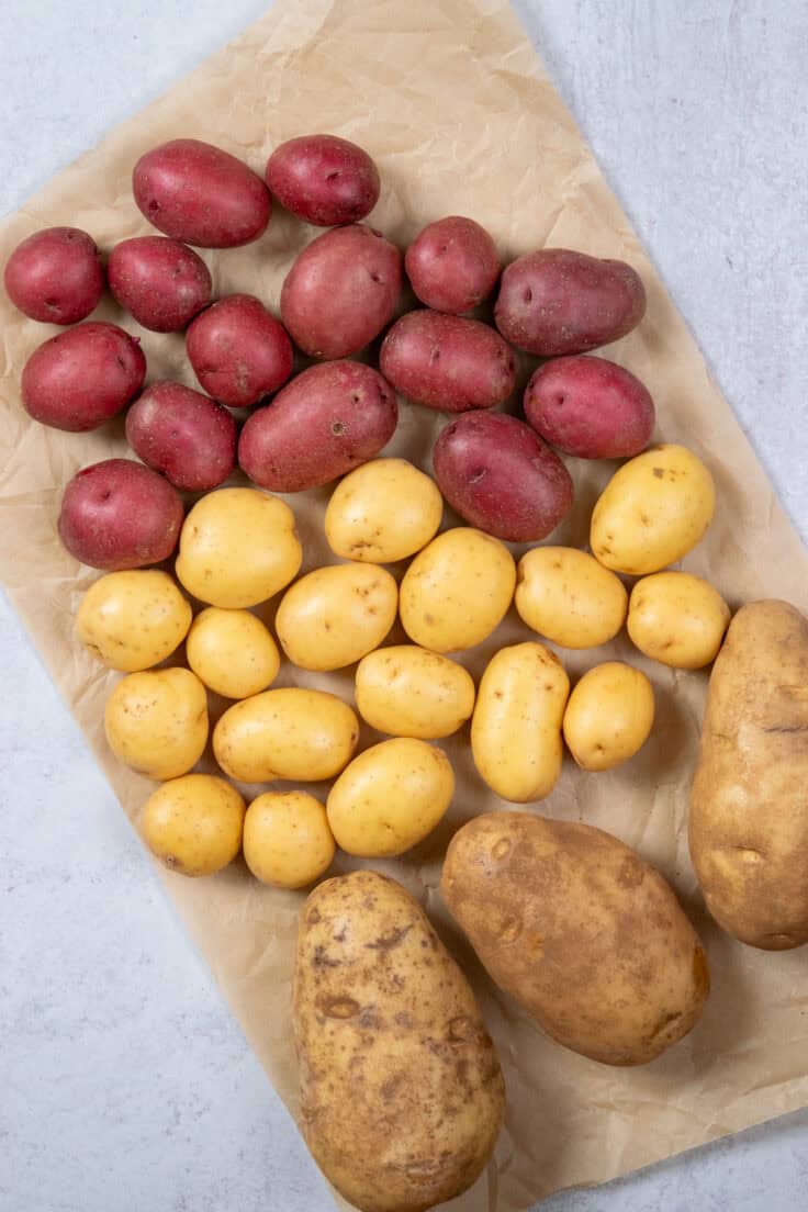 Three types of potatoes in groups on a piece of parchment paper. There are low-starch, high-moisture red potatoes, yellow potatoes and high-starch, low-moisture russet potatoes.