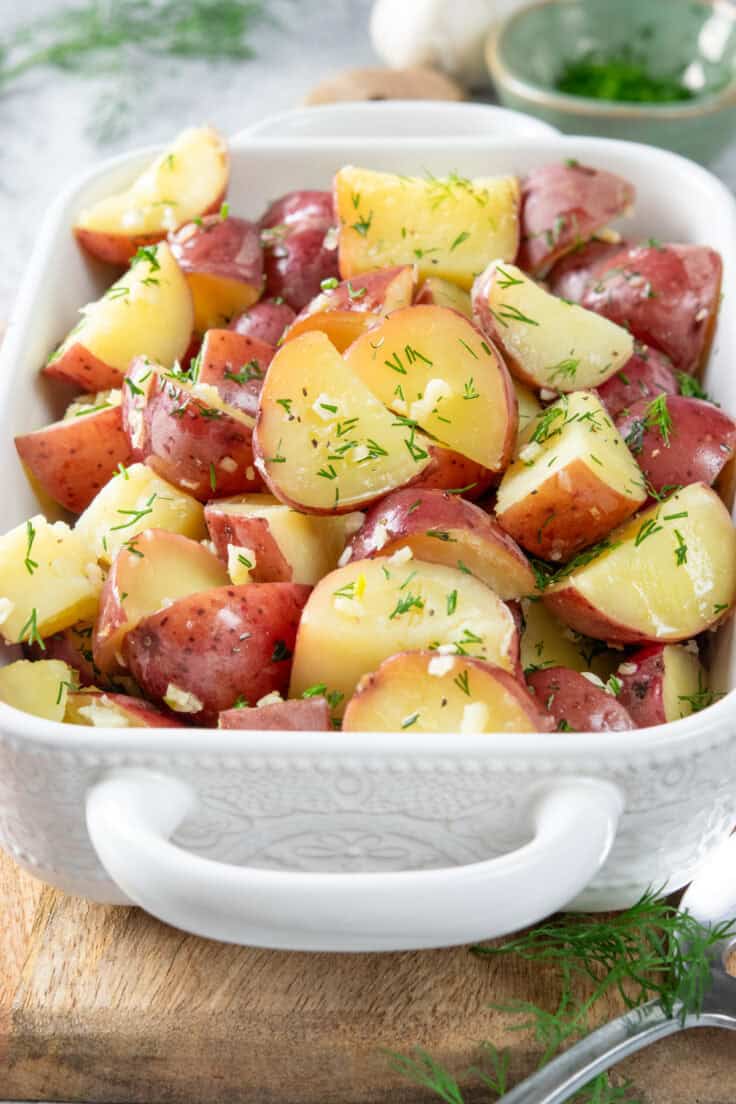 Garlic dill new potatoes in a side dish for serving. You can see minced garlic and bright green minced baby dill on the buttery red potatoes. 