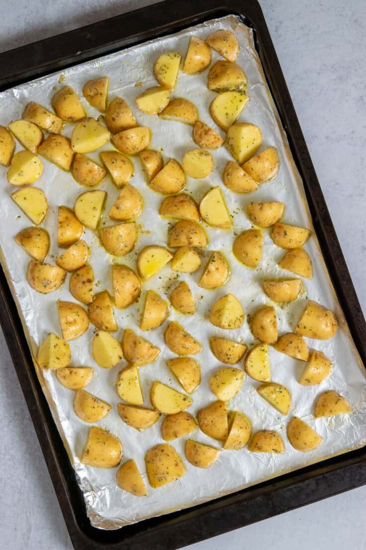 Ranch seasoned yellow new potatoes spread evenly on a large baking sheet ready to go into the oven for roasting.
