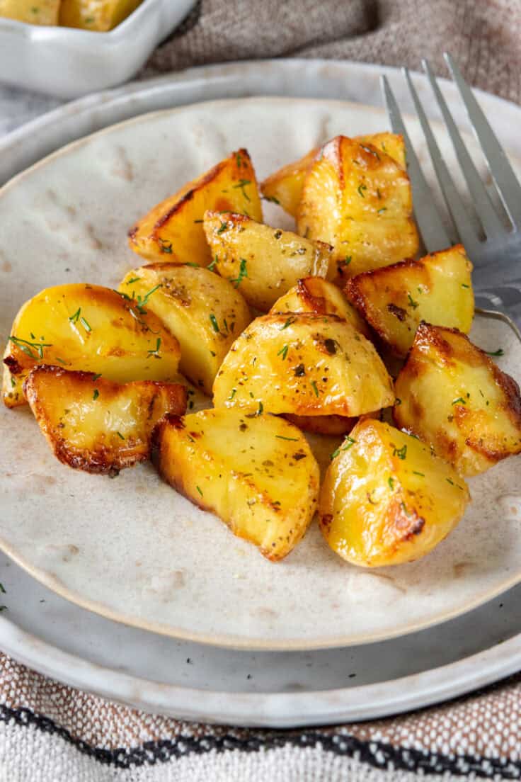 A small side dish with a serving of ranch roasted potatoes. The potatoes are garnished with fresh dill and there is a fork on the plate.