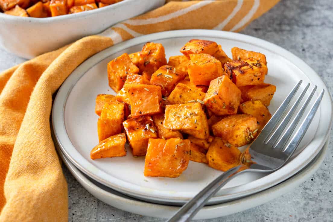 A side dish with roasted sweet potatoes on it. There is a fork on the plate too.