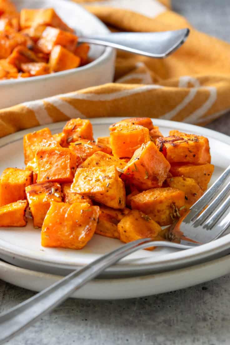A small plate with roasted diced sweet potatoes on it, next to the serving dish.