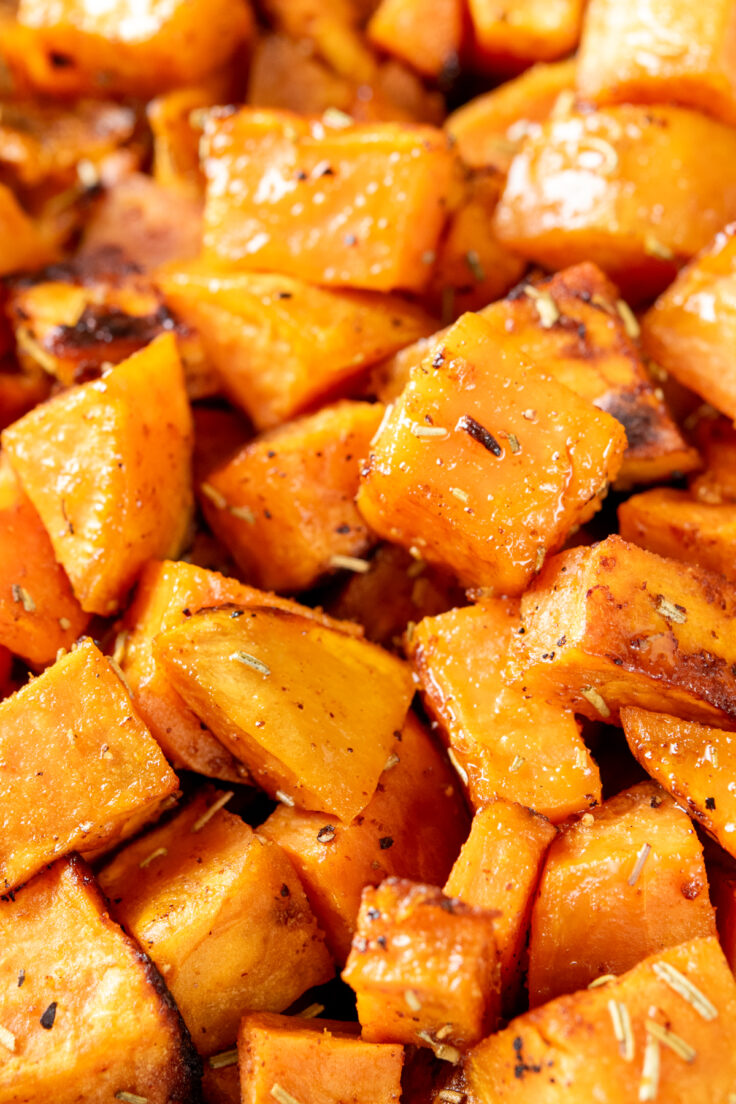 A close-up overhead view of roasted sweet potatoes hot out of the oven. The potatoes are glistening with oil and you can see seasonings and roasted edges.