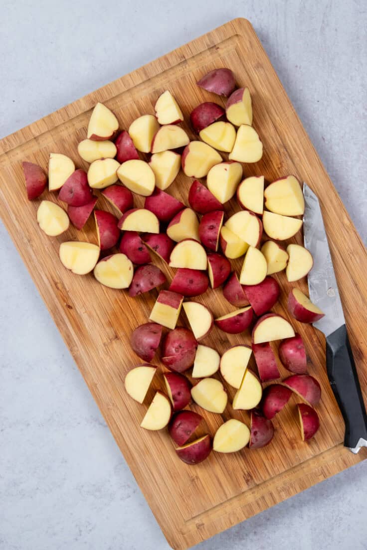 Baby red potatoes on a cutting board with knife that have been cut into small pieces.