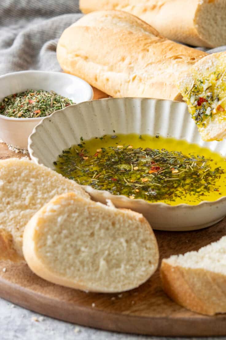 A piece of thick Italian French bread being dipped into the olive oil and seasoning mixture that also has fresh garlic and grated parmesan cheese added to it.