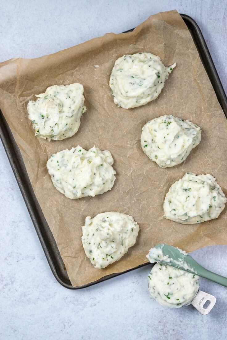 A parchment-lined tray with six serving of mashed potatoes on it in individual scoops, ready to be frozen.