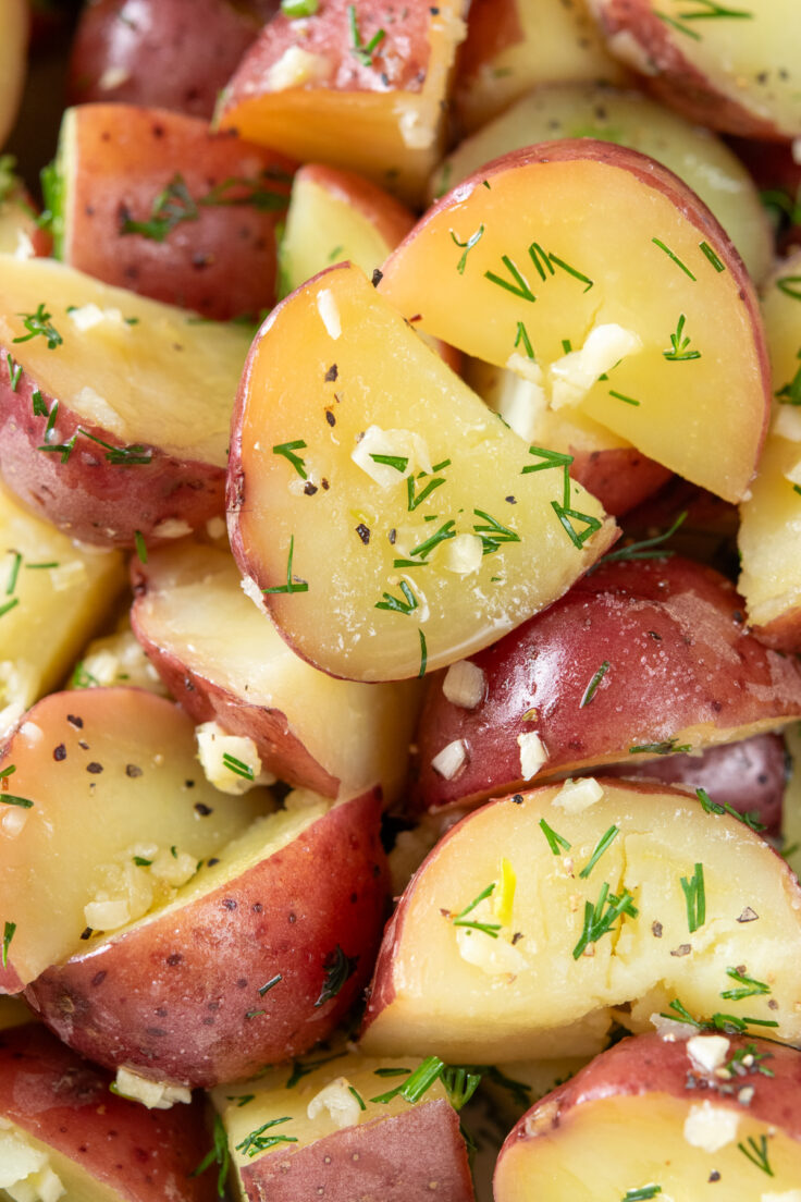 Boiled red new potatoes with butter,  and minced garlic and dill. You can see close-up flecks of the garlic, dill and black pepper on the buttery potatoes.