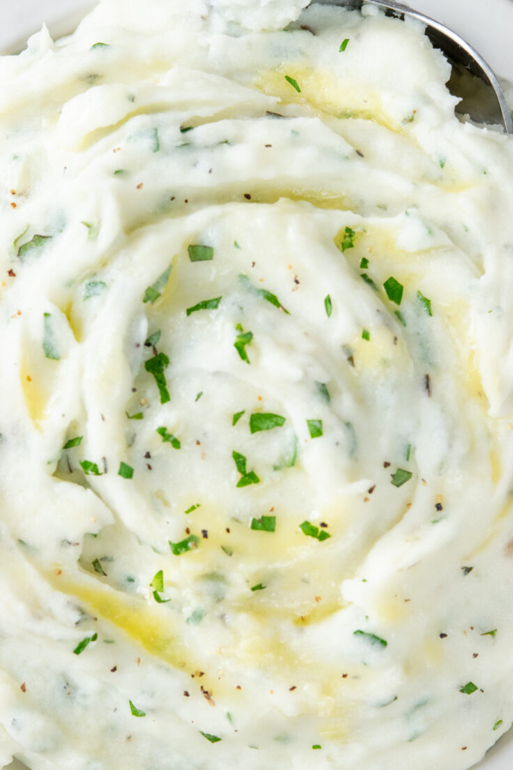 Overhead close-up view of mashed potatoes showing all the flecks of minced fresh herbs, including parsley, thyme and oregano, and lots of butter.