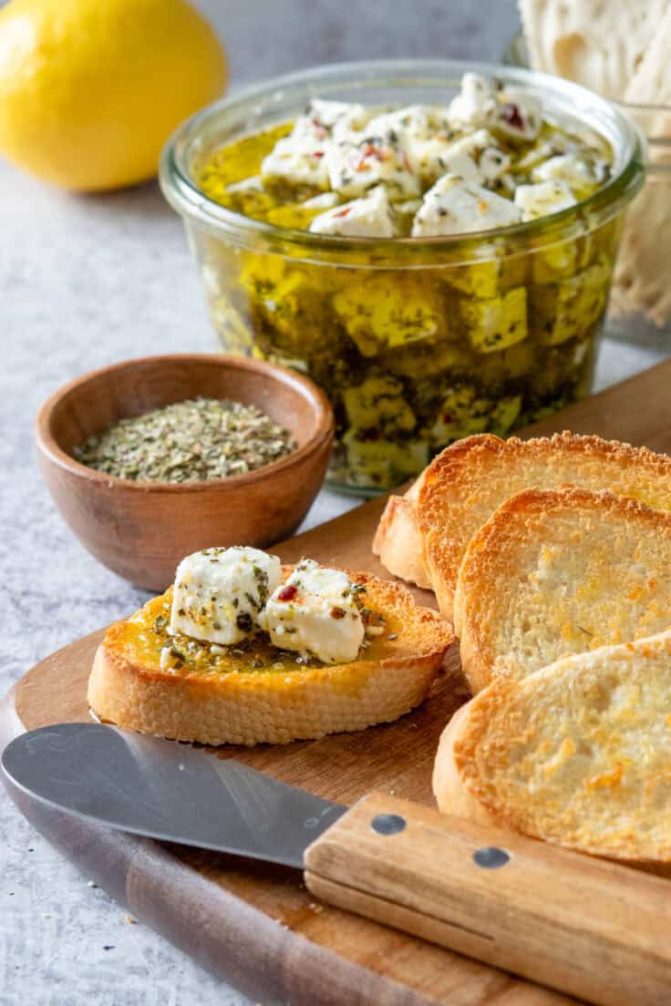Cubes of marinated feta cheese and herby, garlicky olive oil spread on a piece of bread.