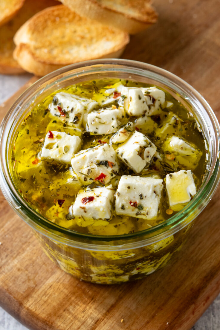 Marinated feta in a bowl with olive oil and lots of herbs and crushed red pepper.