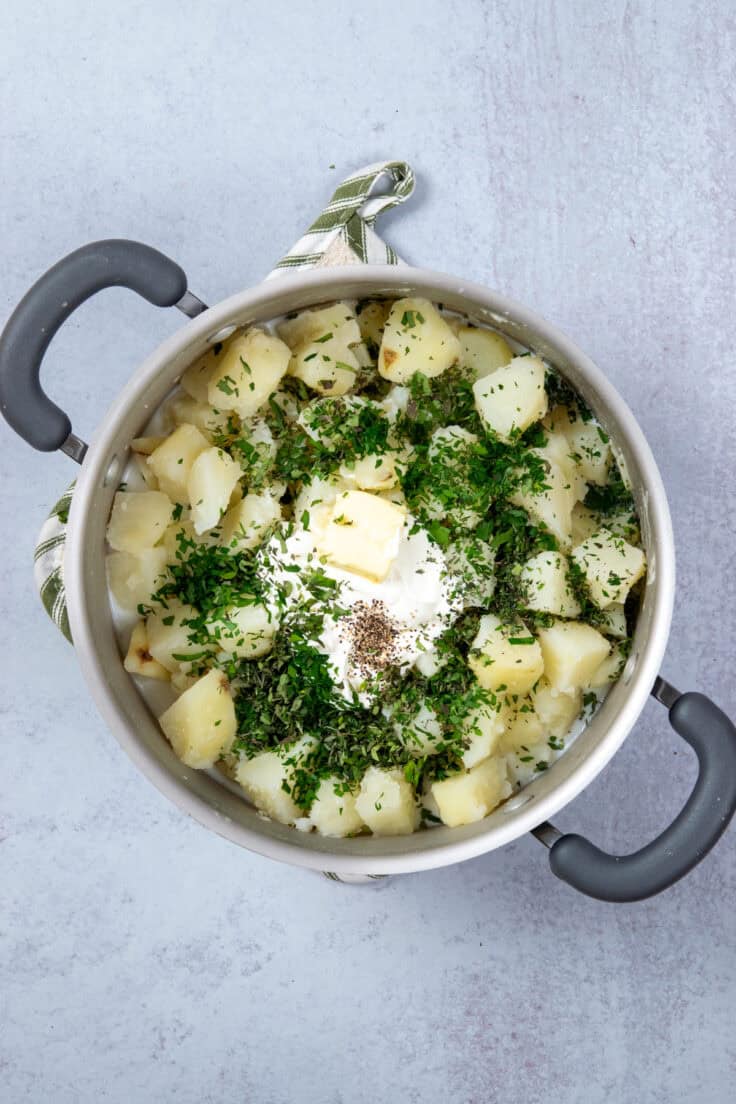 Potatoes returned to pot with herbs, butter, sour cream, milk and salt and pepper added. The mashed potatoes aren't whipped yet.