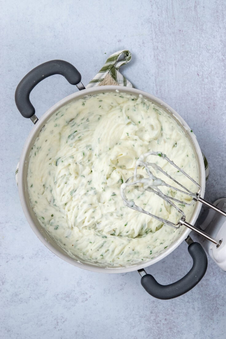 Mashed potatoes in a pot that have been whipped into peaks of fluffy potatoes. The electric mixer and mashed potato-covered beaters are next to the pot.