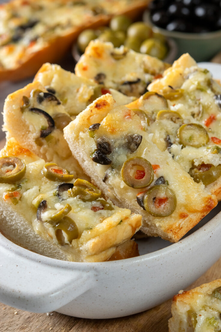 Olive cheese bread cut into thick slices and being served in a small bowl as an appetizer or party snack.