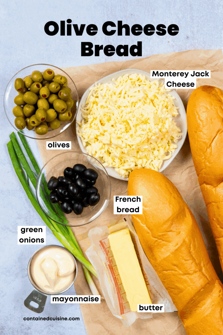 An overhead photo showing labeled ingredients. There's a bowl of green olives with pimentos, a bowl of black olives, two loaves of French bread, two green onions, a half cup measuring cup with mayonnaise, and butter.