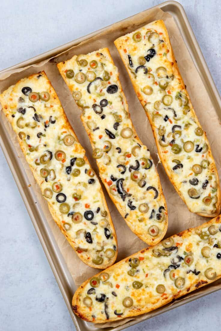 Four large pieces of olive cheese bread baked and still on the tray.