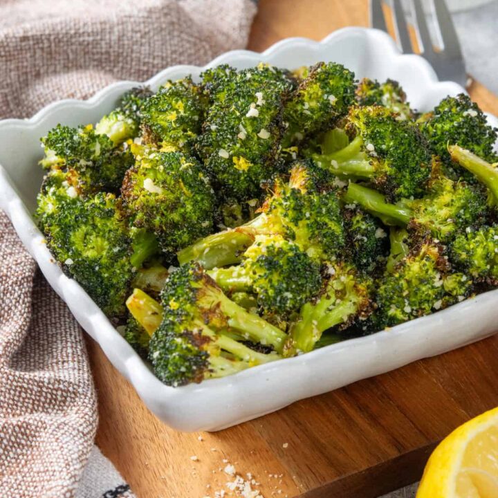 Parmesan roasted broccoli being served in a side dish. You can see grated parmesan on top of the roasted broccoli and some lemon zest.