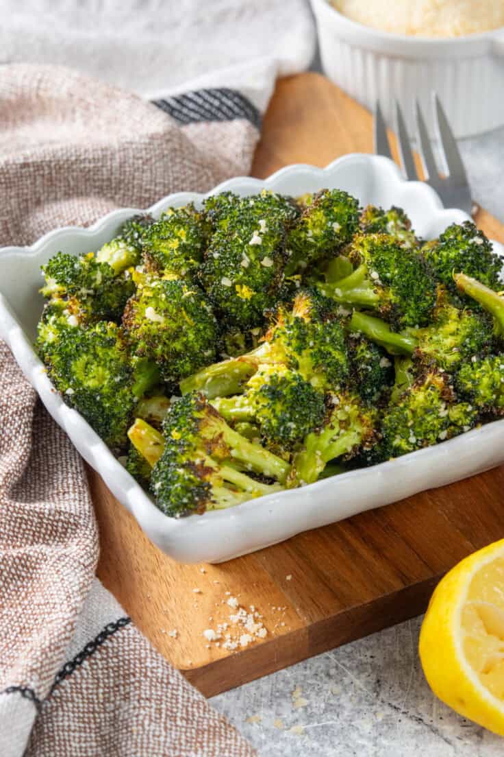 Parmesan roasted broccoli being served in a side dish. You can see grated parmesan on top of the roasted broccoli and some lemon zest.
