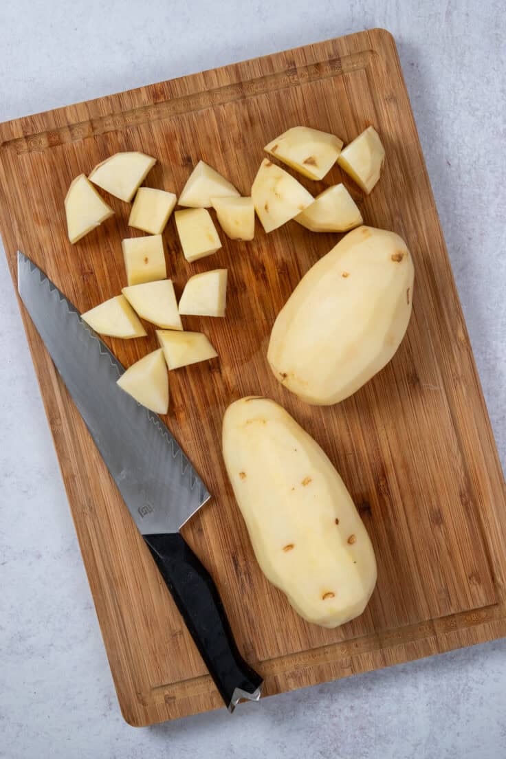 Russet potatoes being cut into cubes on a wood cutting board.