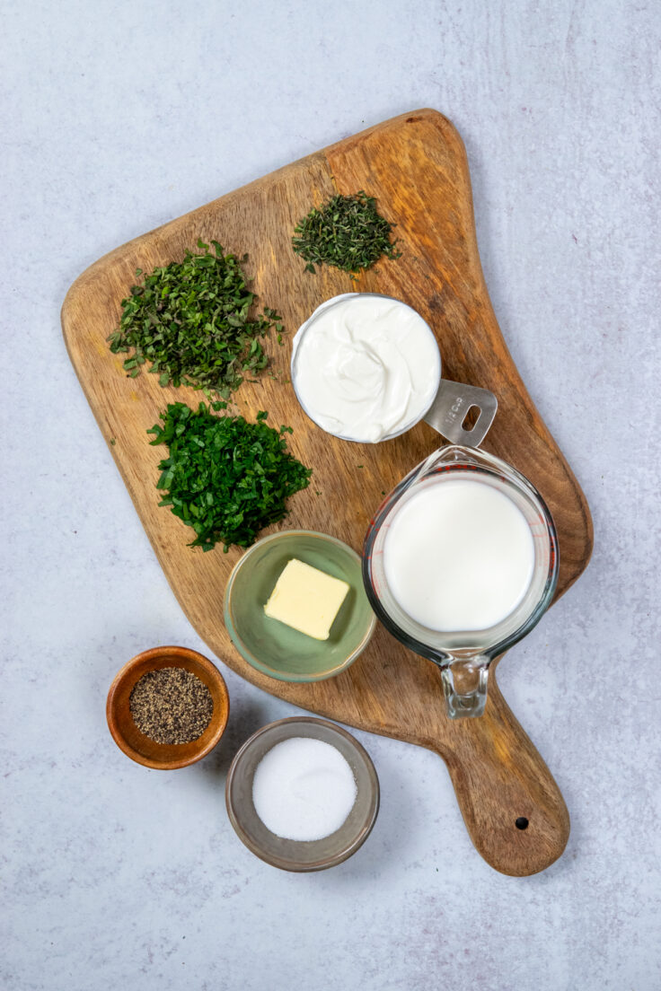 A cutting board with minced herbs, small bowls with salt and pepper, and the butter, sour cream and milk measured out in measuring cups.