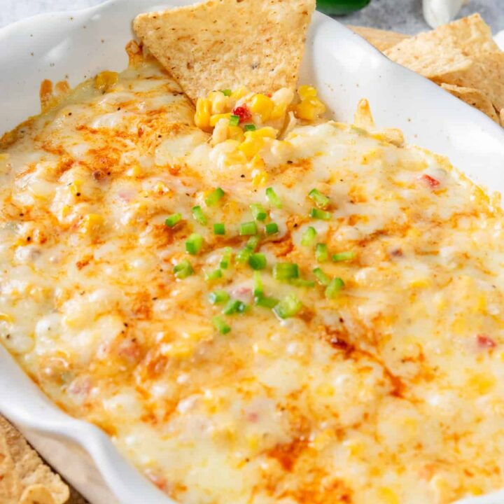 Hot corn dip with melted cheese on top surrounded by corn tortilla chips for dipping.
