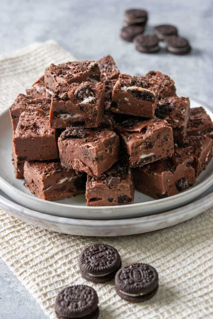 A plate with chunky pieces of Oreo fudge piled on it. Behind the plate are a few mini Oreo cookies scattered around.