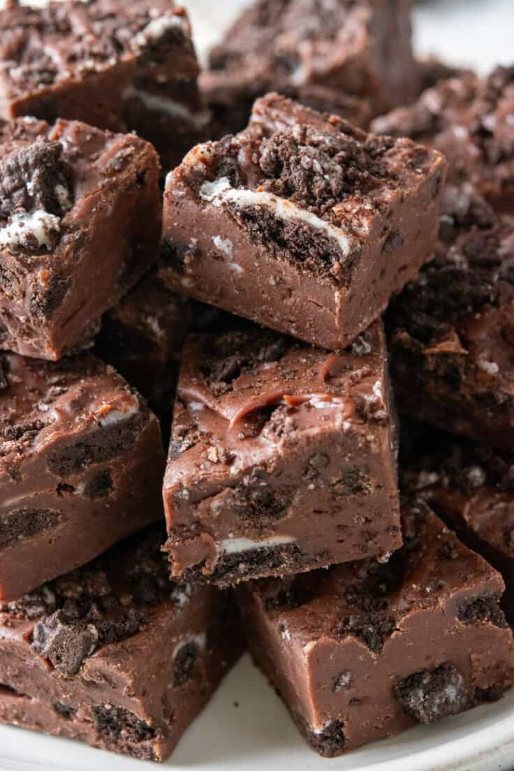 Decadent chcolate Oreo Fudge piled high on a serving tray. You can see the crushed Oreo inside each piece of fudge and on top of it.