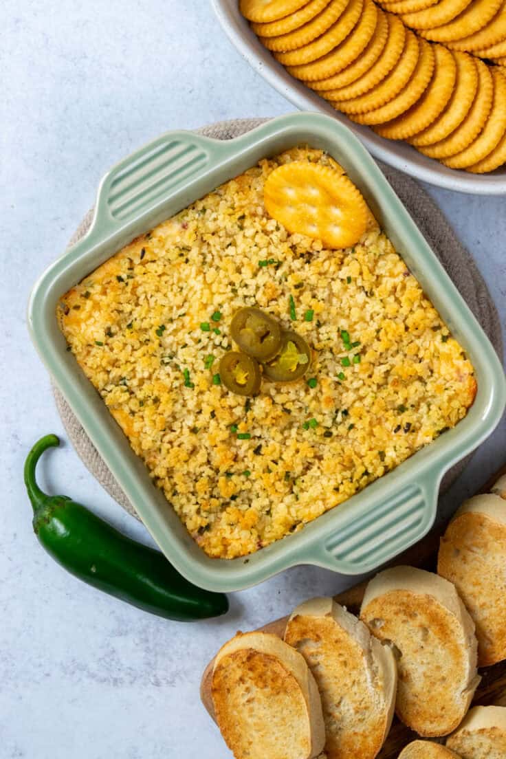 Fresh jalapeño peppers alongside baked jalapeño popper dip, crackers, and sliced French bread ready for serving.